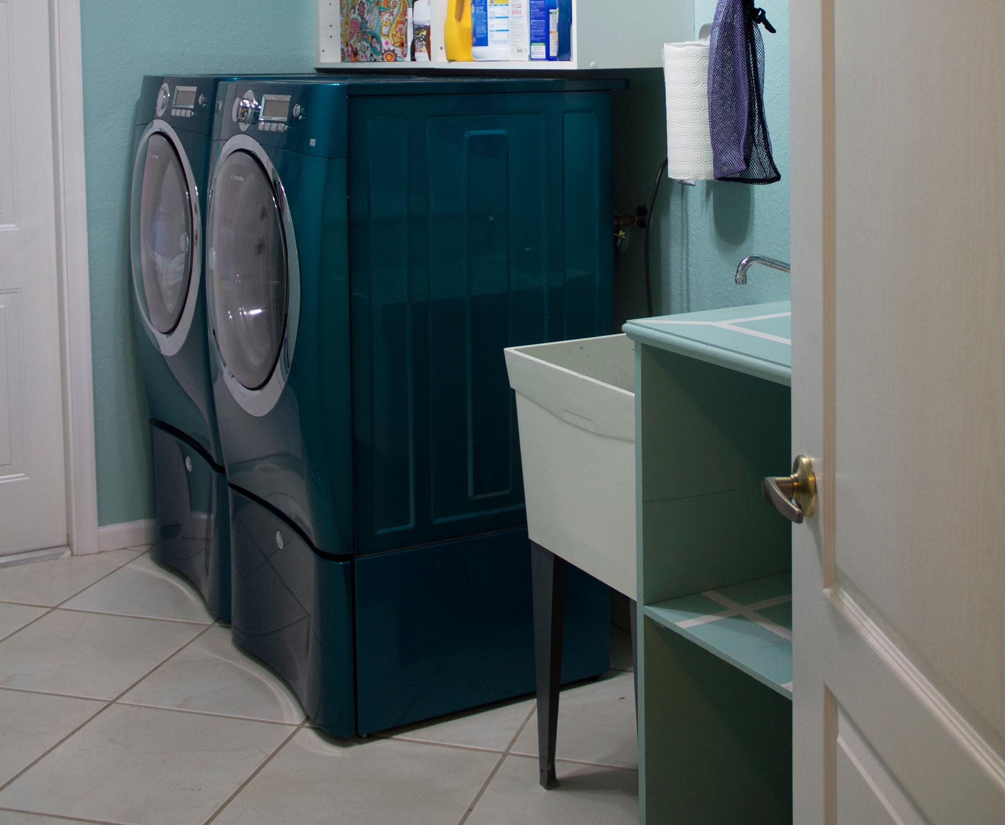 A teal washer and dryer combo in a light-blue laundry room